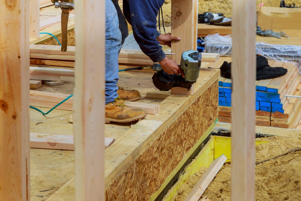 Building contractor worker with a air nail gun nailer working on the corner of the top plate of the first floor walls